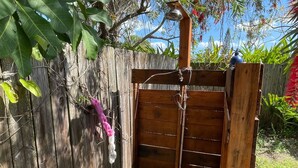 A wooden gate with a metal latch, a wooden post with a blue object on top, and a garden area with green foliage and a wooden fence. - Rock Ridge lll.  Close to everything. (Vero Beach)