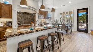 A modern kitchen with granite countertops, wooden bar stools, and pendant lighting.