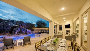 An outdoor dining area with a pool, chairs, and a table set for a meal.