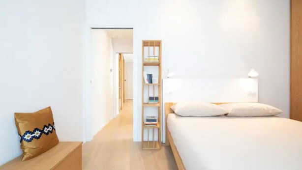 Ein modernes Hotelzimmer mit Bett, Nachttisch, Bücherregal und Bank.