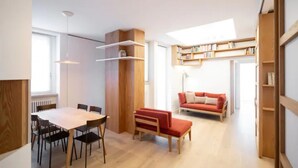 Ein modernes Wohnzimmer mit Esstisch, Stühlen, einem roten Sofa und eingebauten Bücherregalen.