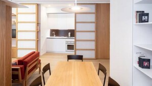 Ein modernes Interieur mit einem Holzes Esstisch, Stühlen, einem roten Sofa, einer Küchenzeile und Einbauschränken.