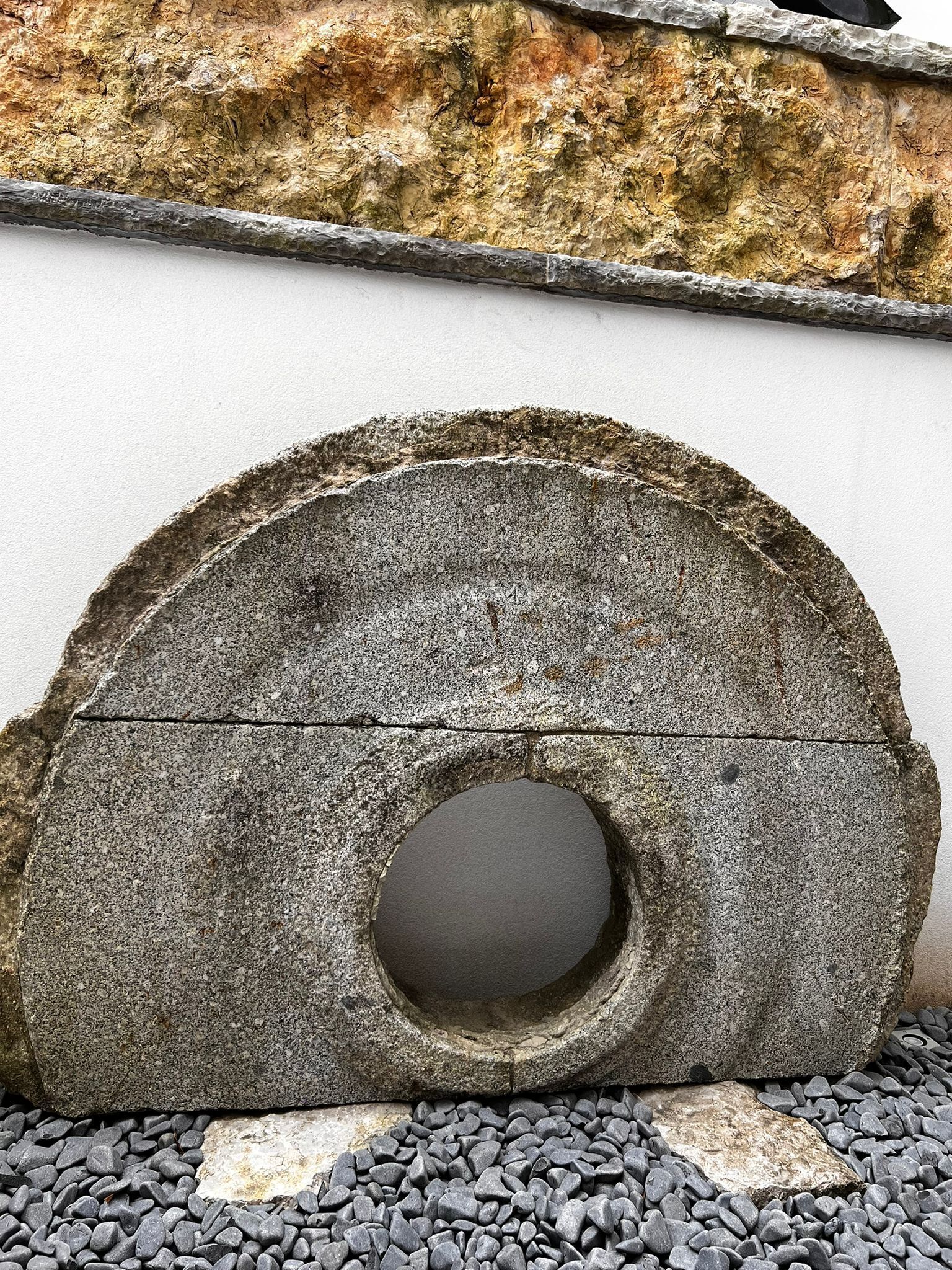 A large, circular stone structure with a central hole, placed on a bed of small, dark stones.