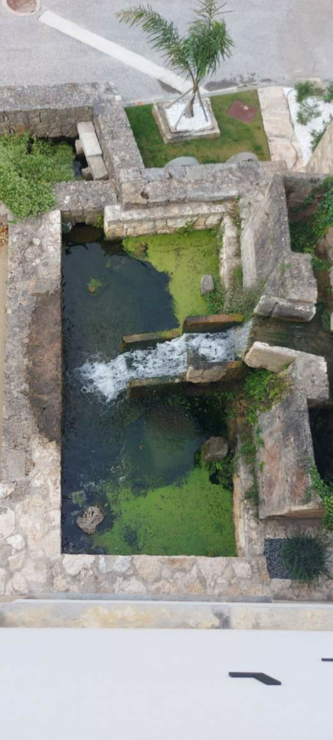 An aerial view of a courtyard with a central water feature, stone walls, and some greenery.