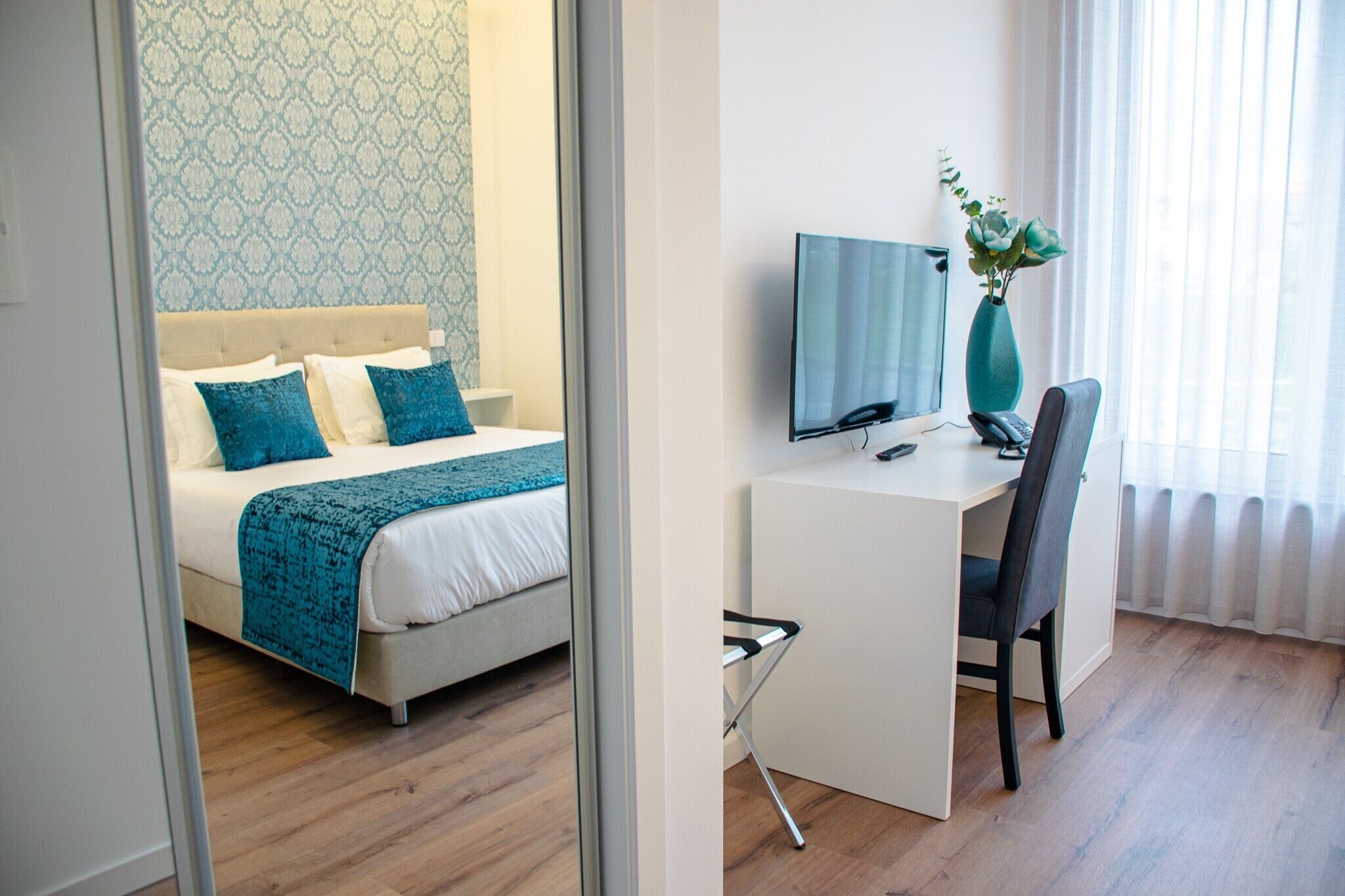 Een hotelkamer met een bed, een bureau, een stoel, een televisie en een vaas met bloemen.