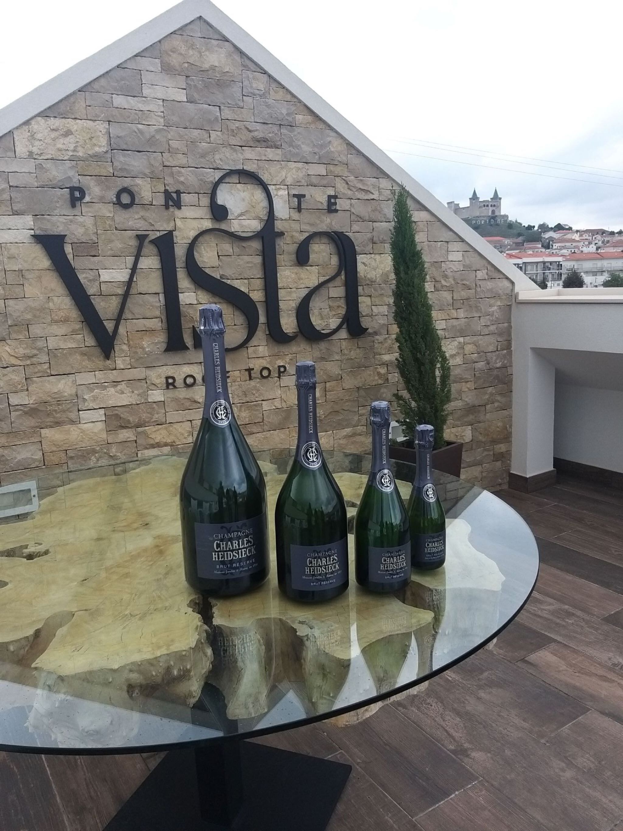 A sign for 'PONTE VISTA' with three bottles of 'Charles Heidsieck' champagne on a glass table.