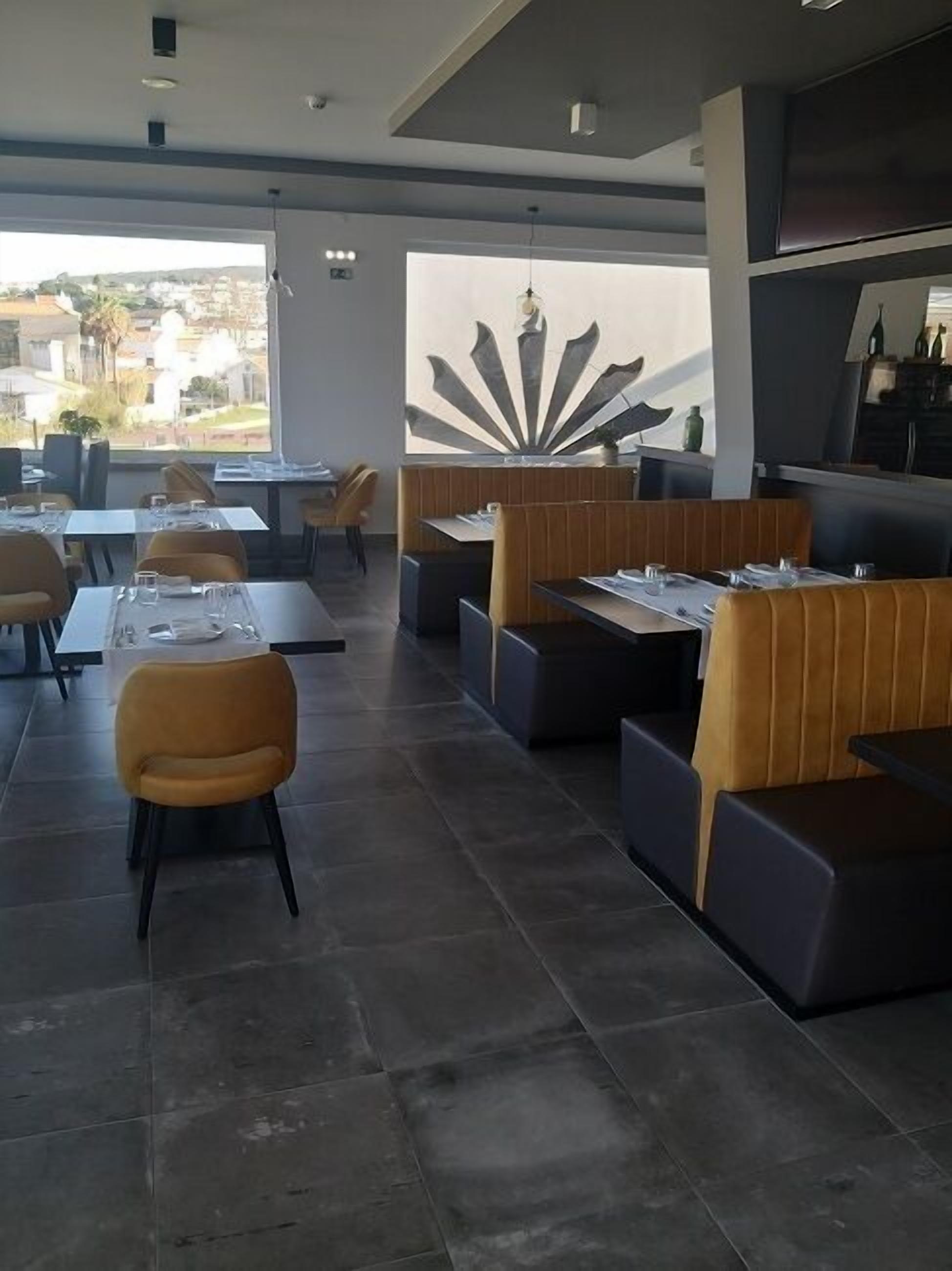 Un ristorante moderno con tavoli alti e banquette, una grande parete decorativa e vista all'esterno.