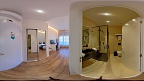 Een moderne hotelkamer met een gebogen houten vloer, een douche met glazen wanden, een apart toilet en een zithoek met een bank en een bijzettafeltje.
