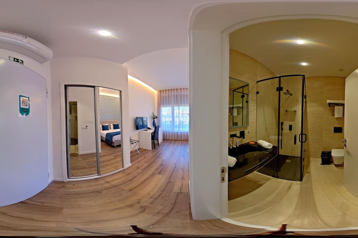 Ett modernt hotellrum med ett böjt trägolv, en dusch med glasväggar, ett separat badrum och en sittgrupp med en soffa och ett litet bord.