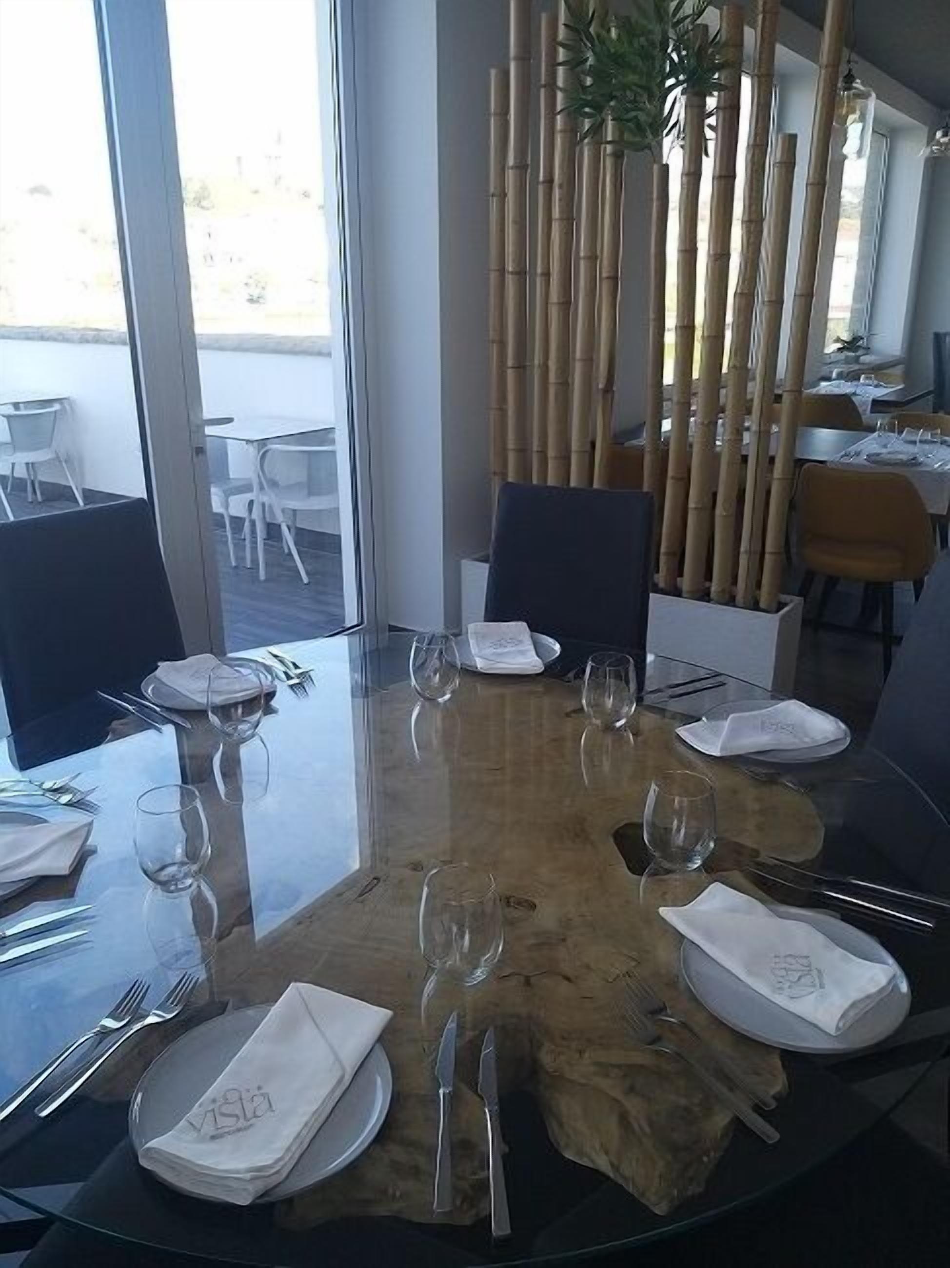 Une table à manger pour six personnes, avec un plateau en verre, entourée de chaises, dans un restaurant moderne offrant une vue sur l’extérieur.