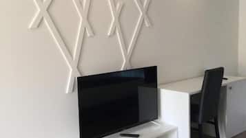 A modern living room with a flat-screen TV on a white entertainment unit, a desk with a chair, and a decorative wall panel.
