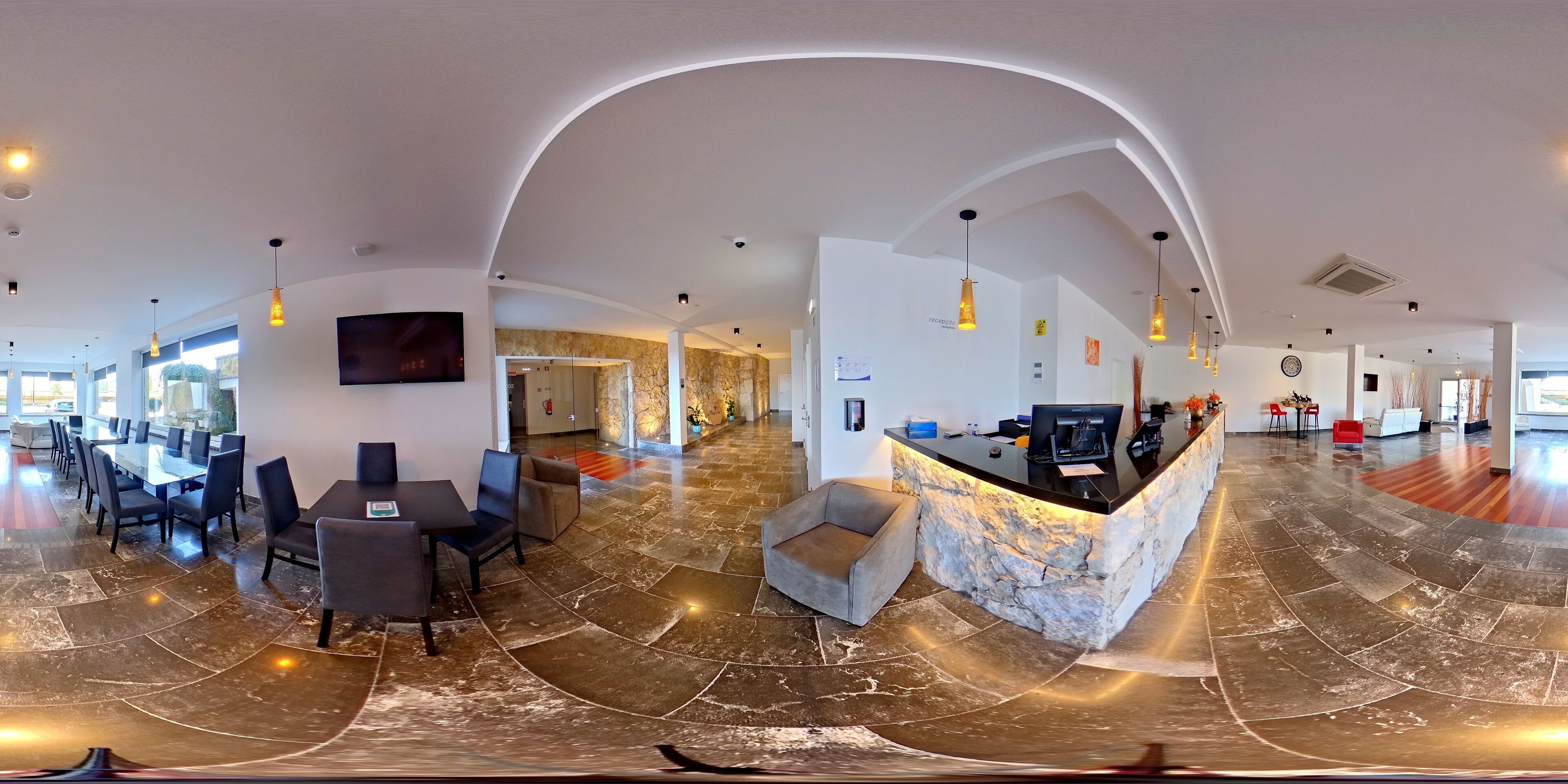 A panoramic view of a hotel lobby with a reception desk, seating area, and a dining space.