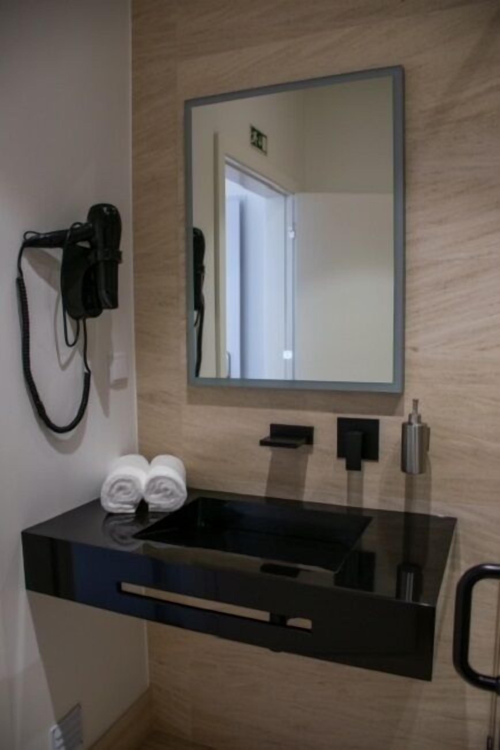 Un baño moderno con un lavamanos negro, un espejo grande y un secador de pelo en la pared.