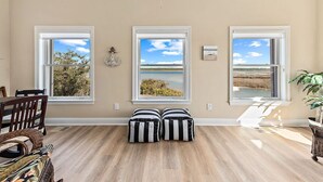 A room with three windows, a dining table with chairs, and two striped cushions. - Calvert Castle, Elevator, Golf cart, Beach ,Pool (gulf shores)