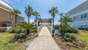 A pathway leading to a gazebo surrounded by palm trees and a garden with various plants. - Calvert Castle, Elevator, Golf cart, Beach ,Pool (gulf shores)