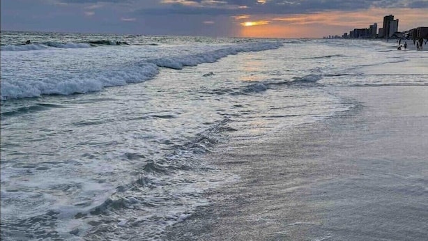 A beach with waves, a sunset, and a distant city skyline. - Snowbird Retreat! Escape Winter and Save Today (Panama City Beach)