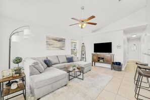 Un salon comprenant un canapé d’angle, une table basse, un téléviseur et un ventilateur de plafond.