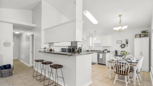 A modern kitchen with a central island, bar stools, a dining area with chairs, and a chandelier. - Snowbird Retreat! Escape Winter and Save Today (Panama City Beach)