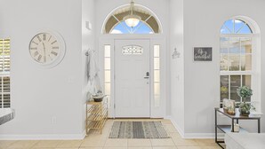 A clean, well-lit entrance with a white door, a clock, and a decorative wall piece. - Snowbird Retreat! Escape Winter and Save Today (Panama City Beach)