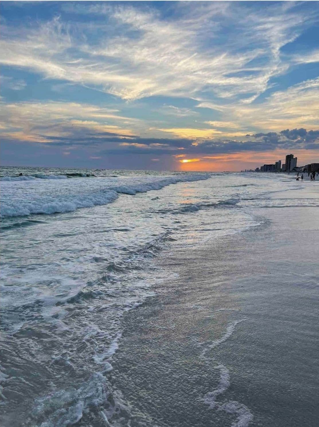 Een strand met golven, een zonsondergang en een verafgelegen stadshemelbeeld.