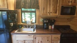 A kitchen with wooden cabinets, a sink, a stove, and a microwave. - Cozy Log Cabin at Warrior Ethos Farm (Cooperstown)
