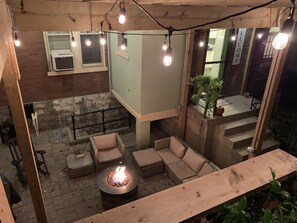 An outdoor patio area with a fire pit, seating, and string lights.