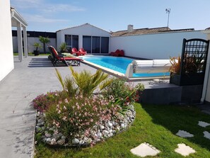 A backyard with a swimming pool, red lounge chairs, and a garden with pink flowers and rocks.