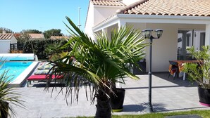 A pool area with lounge chairs, a dining table with chairs, and a potted palm tree. - Villa "Le Paradis Bleu" Heated pool and beach 200 m'away (Saint-Gilles-Croix-de-Vie)
