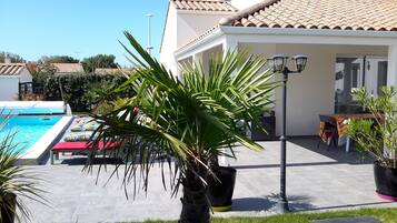 A pool area with lounge chairs, a dining table with chairs, and a potted palm tree.