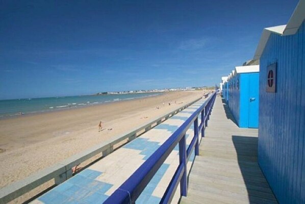 A beachside walkway with a wooden deck and a blue building with a door.