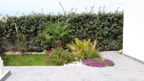 A landscaped garden with a variety of plants and flowers, a neatly trimmed hedge, and a paved patio area.