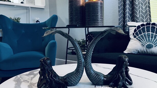 Una sala de estar moderna con una mesa de centro redonda de mármol, dos velas negras sobre un soporte negro, un sofá azul y un sillón negro.