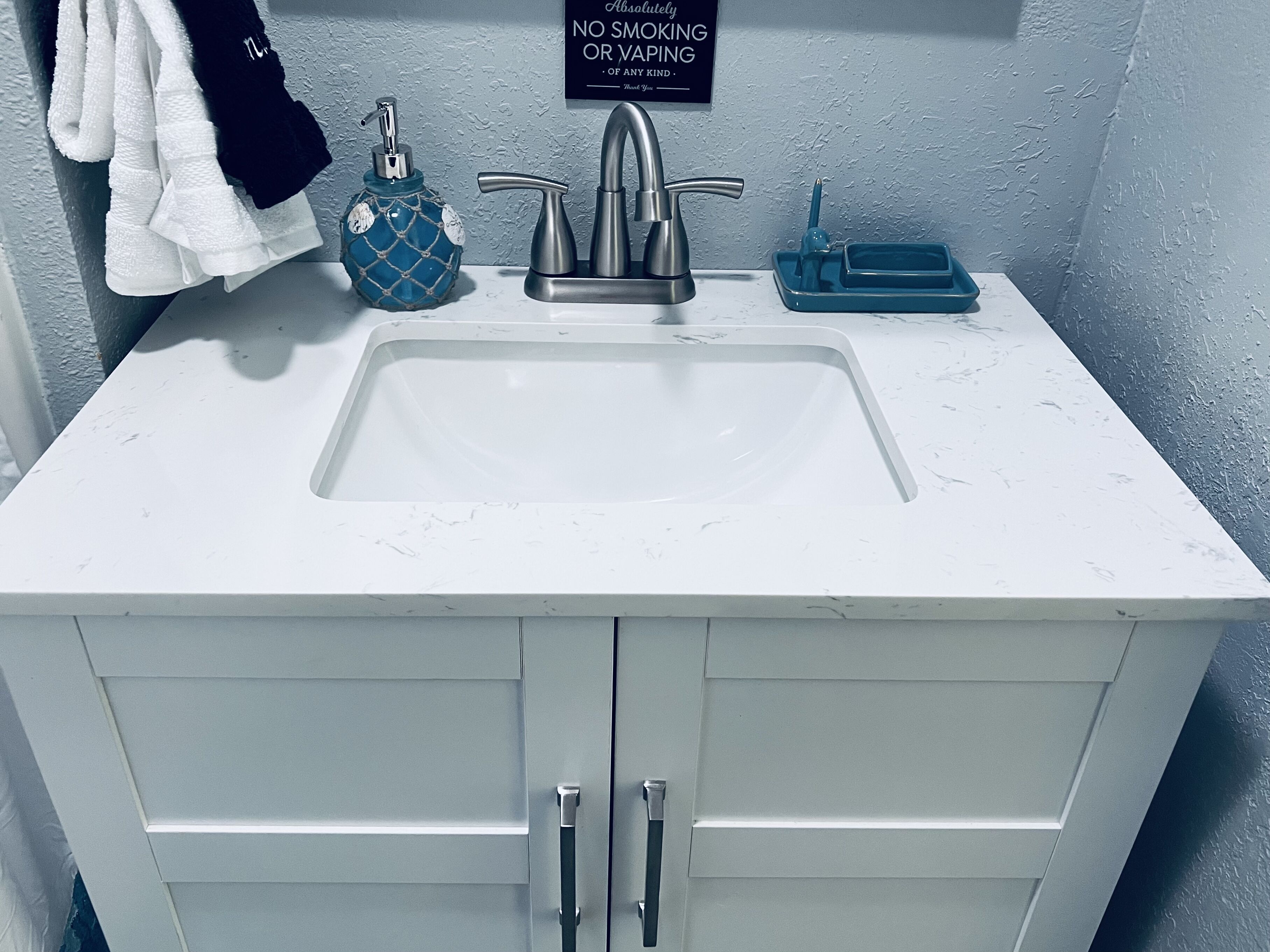 A bathroom with a white sink, a soap dispenser, and a 'No Smoking' sign.