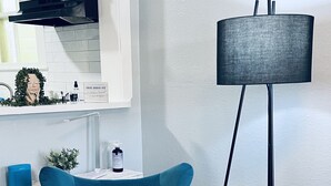 Un salón moderno con un sillón azul verdoso, una lámpara de pie negra y una mesita auxiliar con una planta.