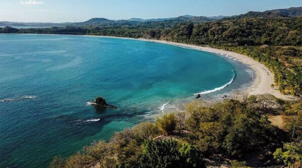 Un paysage côtier avec une plage, des eaux turquoise et limpides, et une végétation luxuriante.
