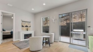 Un salon moderne doté d’une cheminée, d’un coin salon et d’une porte-fenêtre coulissante donnant sur un espace barbecue extérieur.