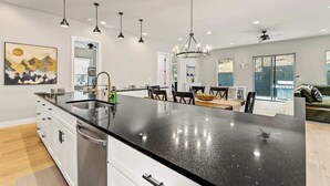 Une cuisine moderne avec un plan de travail noir, des armoires blanches et des luminaires suspendus.