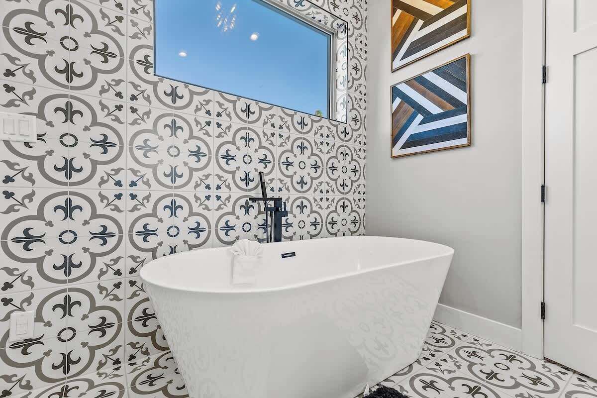 A bathroom with a freestanding bathtub, patterned tiles, a mirror, and framed artwork on the wall.