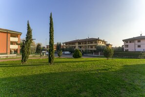 A residential area with a grassy lawn, tall trees, and multi-story buildings with balconies.