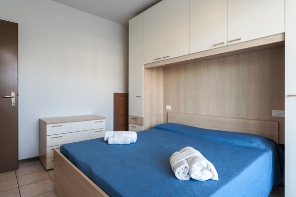 A bedroom with a bed, a wooden wardrobe, a bedside table, and a nightstand.