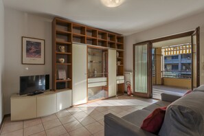 Una sala de estar con televisor, sofá, mueble y puerta corrediza de vidrio que da a un balcón.