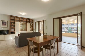 A living room with a sofa, a wooden dining table with chairs, a television, and a bookshelf.