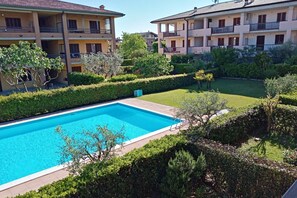 A swimming pool surrounded by well-maintained hedges and a multi-story building with balconies.
