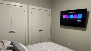 Un dormitorio con dos armarios blancos, una cama con ropa de cama estampada y un televisor de pared mostrando opciones de Netflix.