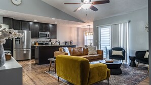 A modern kitchen with dark cabinets, a stainless steel refrigerator, and a microwave. There is a dining area with a yellow sofa and a black armchair. - Isle of the Pines, 1 mile from The Village of Pinehurst! (Pinehurst)