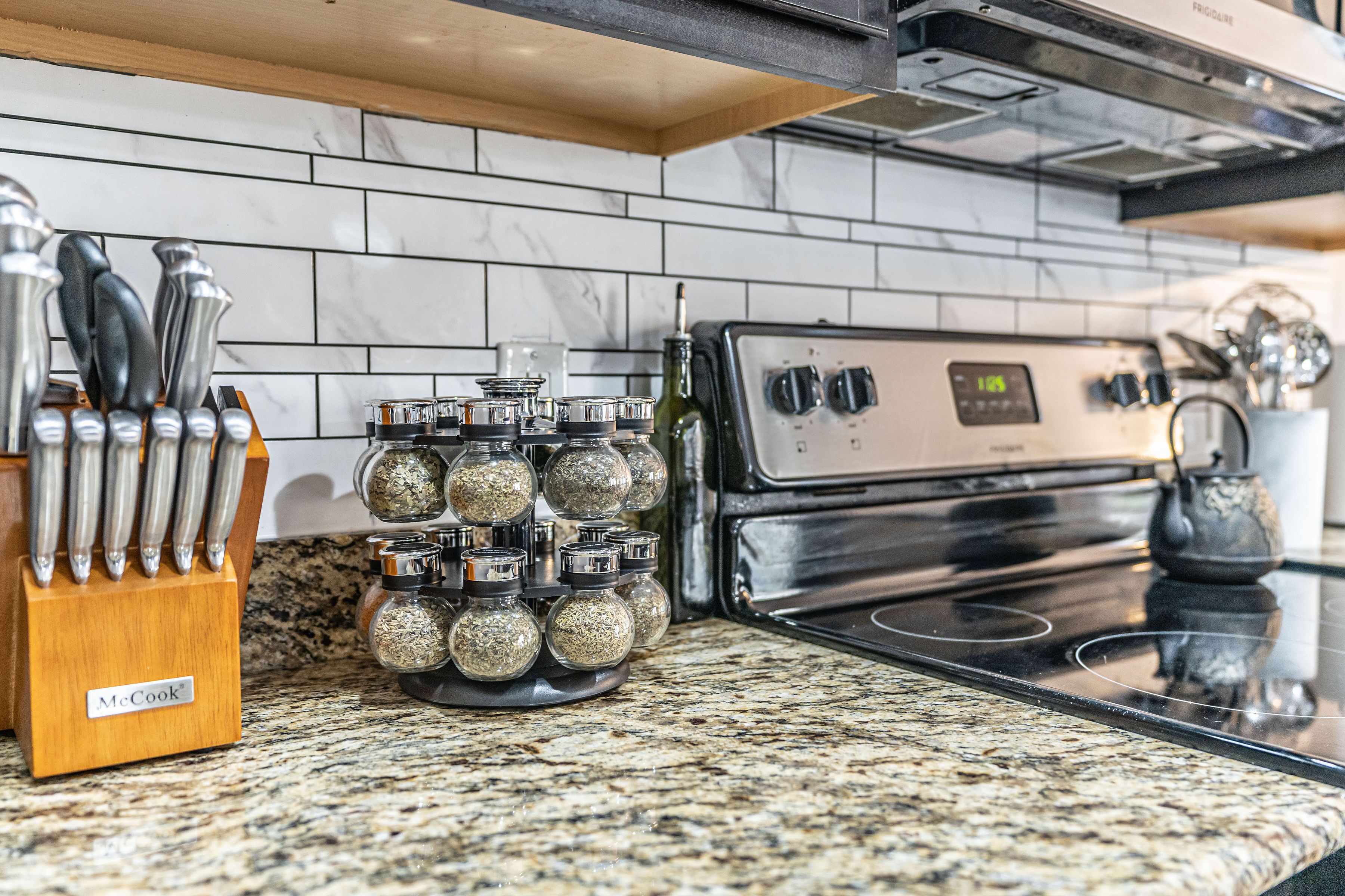A kitchen with a granite countertop, a stainless steel stove, and a spice rack with glass jars.