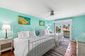 Ein Schlafzimmer mit zwei Betten, einem Deckenventilator und einem Balkon mit Blick auf Palmen.