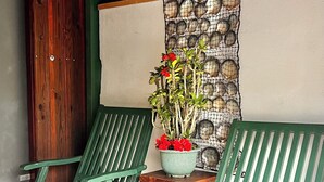 Dos sillones de relax verdes con cojines estampados, una planta en maceta con flores rojas y una pared de piedra con un cuadro enmarcado.