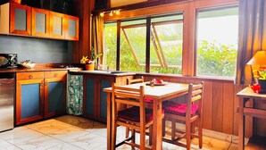Una cocina con armarios de madera, una mesa de comedor con sillas, un lavabo y un ventanal con cortinas.