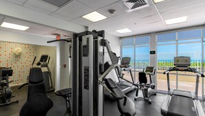 Ett gym med olika typer av träningsutrustning, ett löpband och utsikt över naturen genom stora fönster.